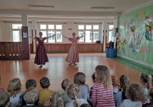 Dzieci siedzą na ławce i oglądają taneczny występ.