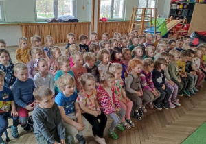 Dzieci siedzą na ławce i oglądają taneczny występ.