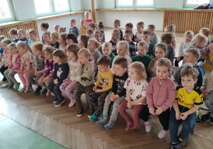 Dzieci siedzą na ławce i czekają na występ.