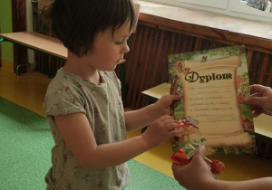 Nauczyciel wręcza dziewczynce dyplom za udział w konkursie.