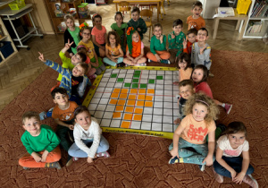 Dzieci siedzą na dywanie i prezentują ułożoną marchewkę na macie do kodowania.