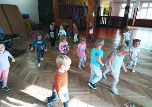 Dzieci na sali gimnastycznej biegają w rytm muzyki.