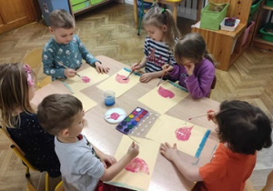 Dzieci malują farbami flamingi.